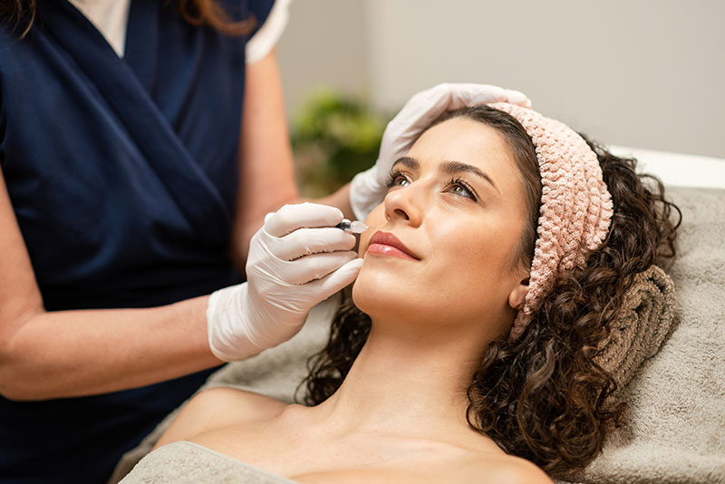 woman receiving lip filler injection from a professional aesthetician.